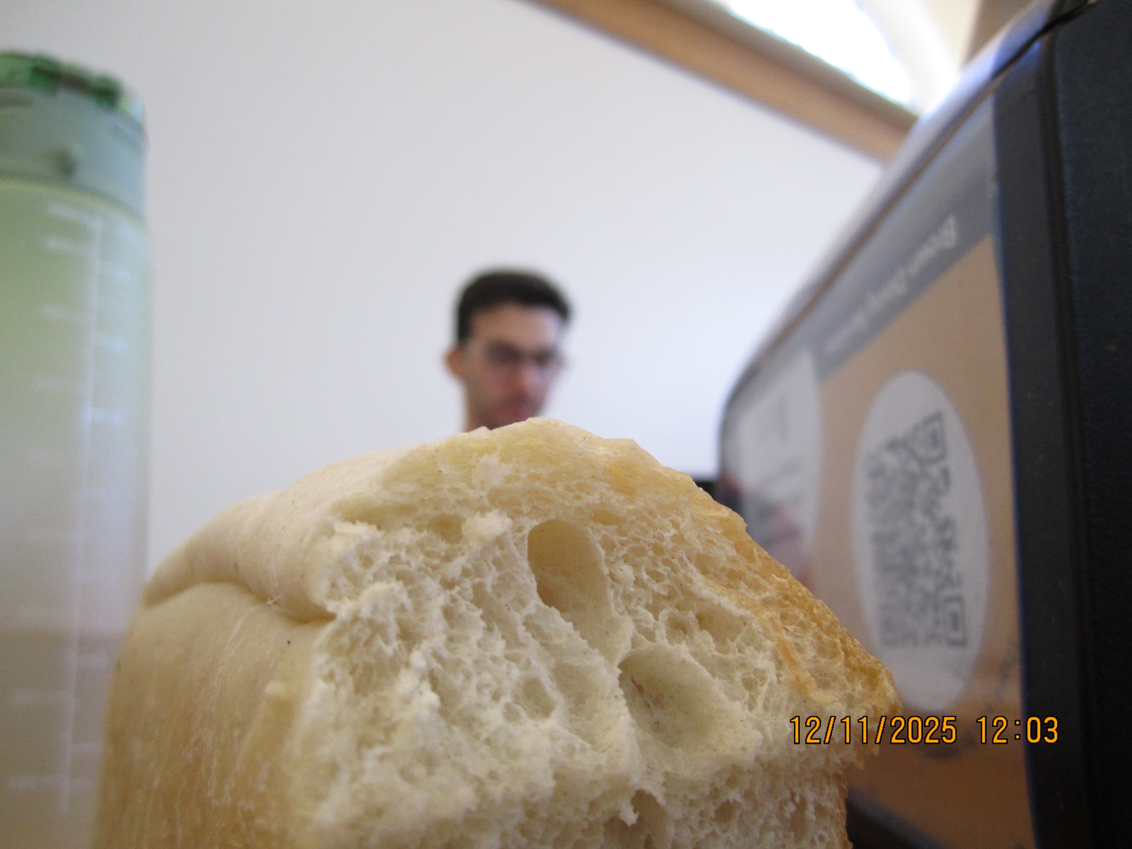 Up-close photo of bread, with a water bottle on one side and a napkin dispenser on the other. Alex's head, which is out of focus, pokes up from behind the bread.