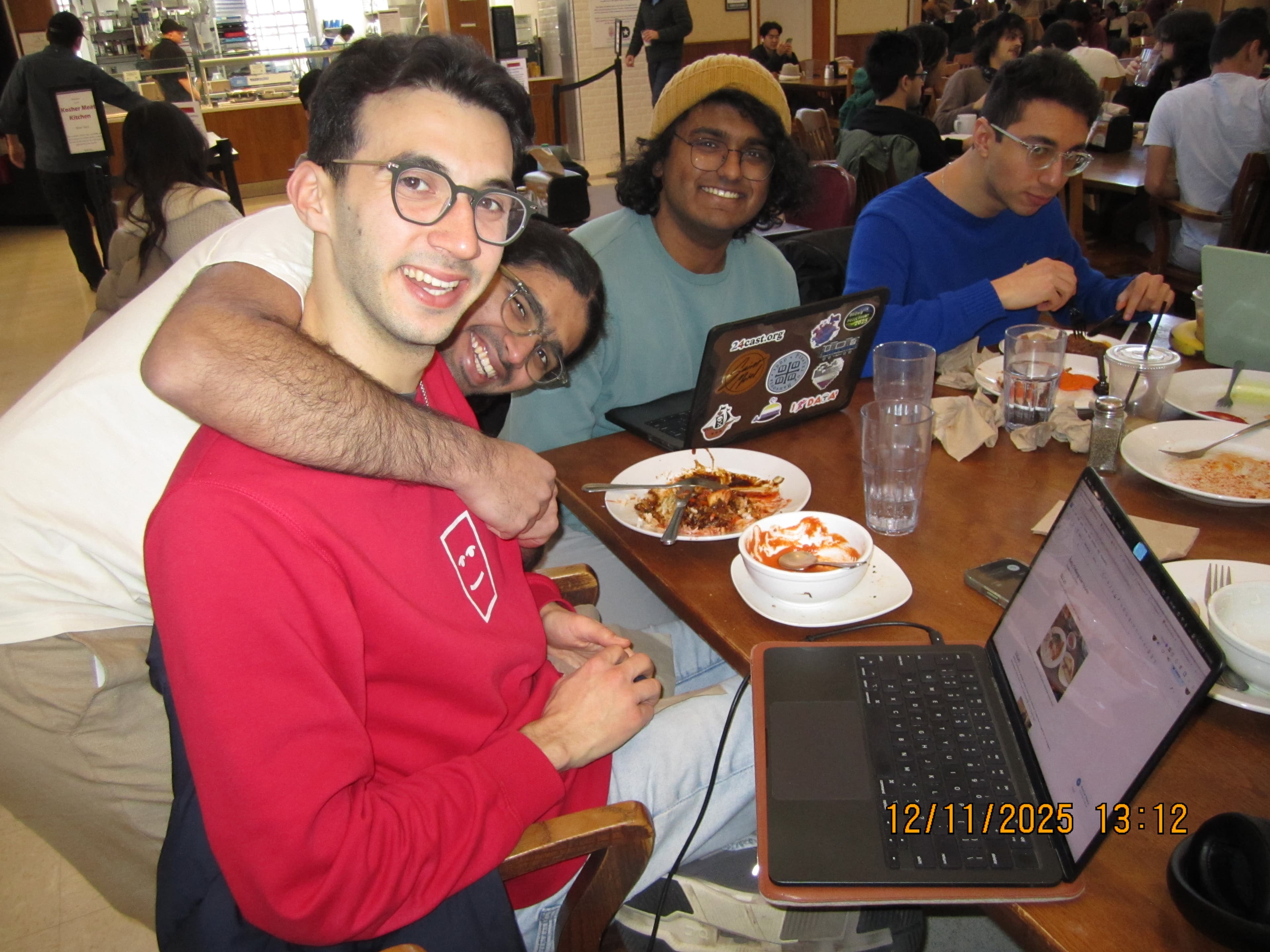 Alex, Atharva, Chai, and Omeed gathered around the table with food-filled plates and Alex's laptop.